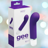 The VeDO 'Gee' Mini G-Spot Rechargeable Waterproof Vibrator in indigo, designed with a curved tip for optimal G-spot stimulation, is showcased alongside its packaging. The package prominently displays the product image and highlights features such as "gee mini vibe" and "10 vibration modes," all set against a softly blurred background with circular light spots.